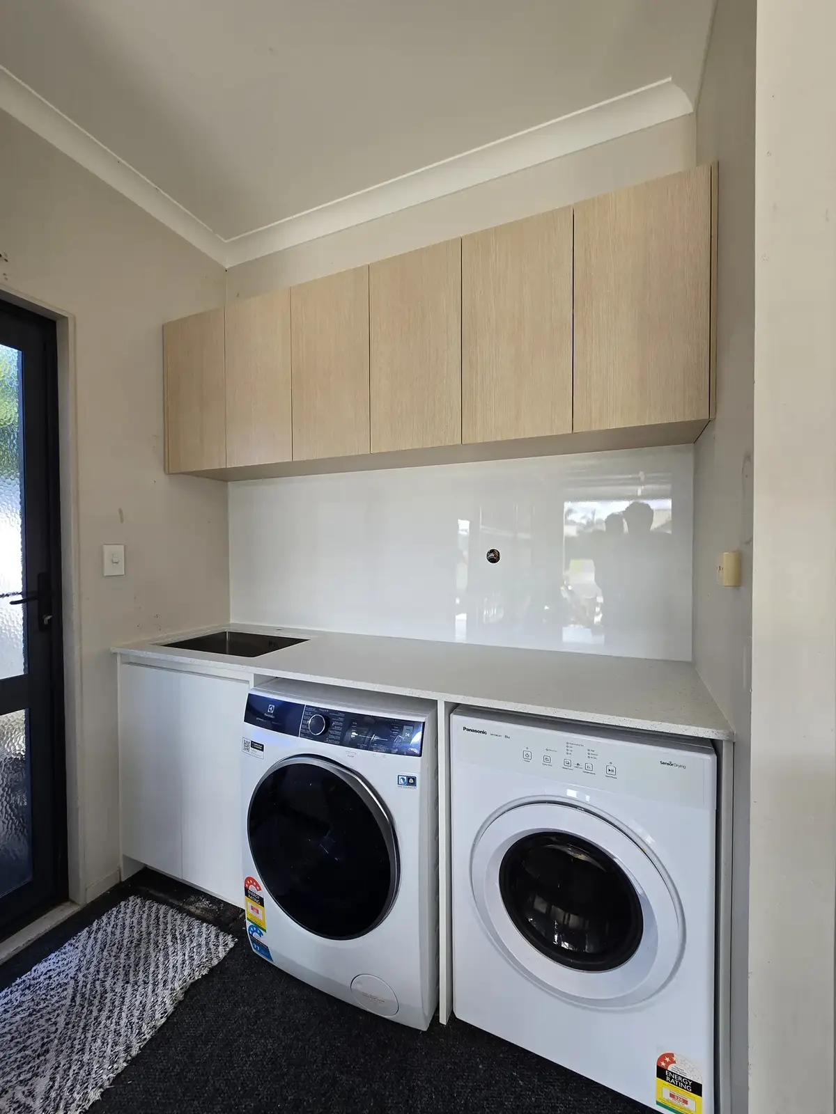 Oak laundry fit-out with stacked washer and dryer and custom cabinetry by Flow Joinery